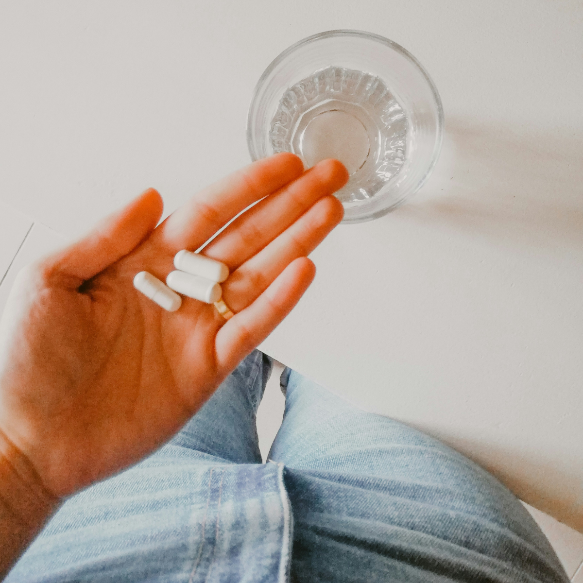 A hand holding a few vitamin capsules and a glass of water